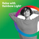 Young adult woman relaxing with hands behind her head, smiling with eyes closed, next to 'Relax with Rainbow Light®' text.