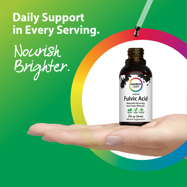 An adult female hand holds a Rainbow Light Fulvic Acid liquid bottle.