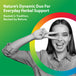Young adult female smiling and making a peace sign over her eyes, against a green and rainbow background.